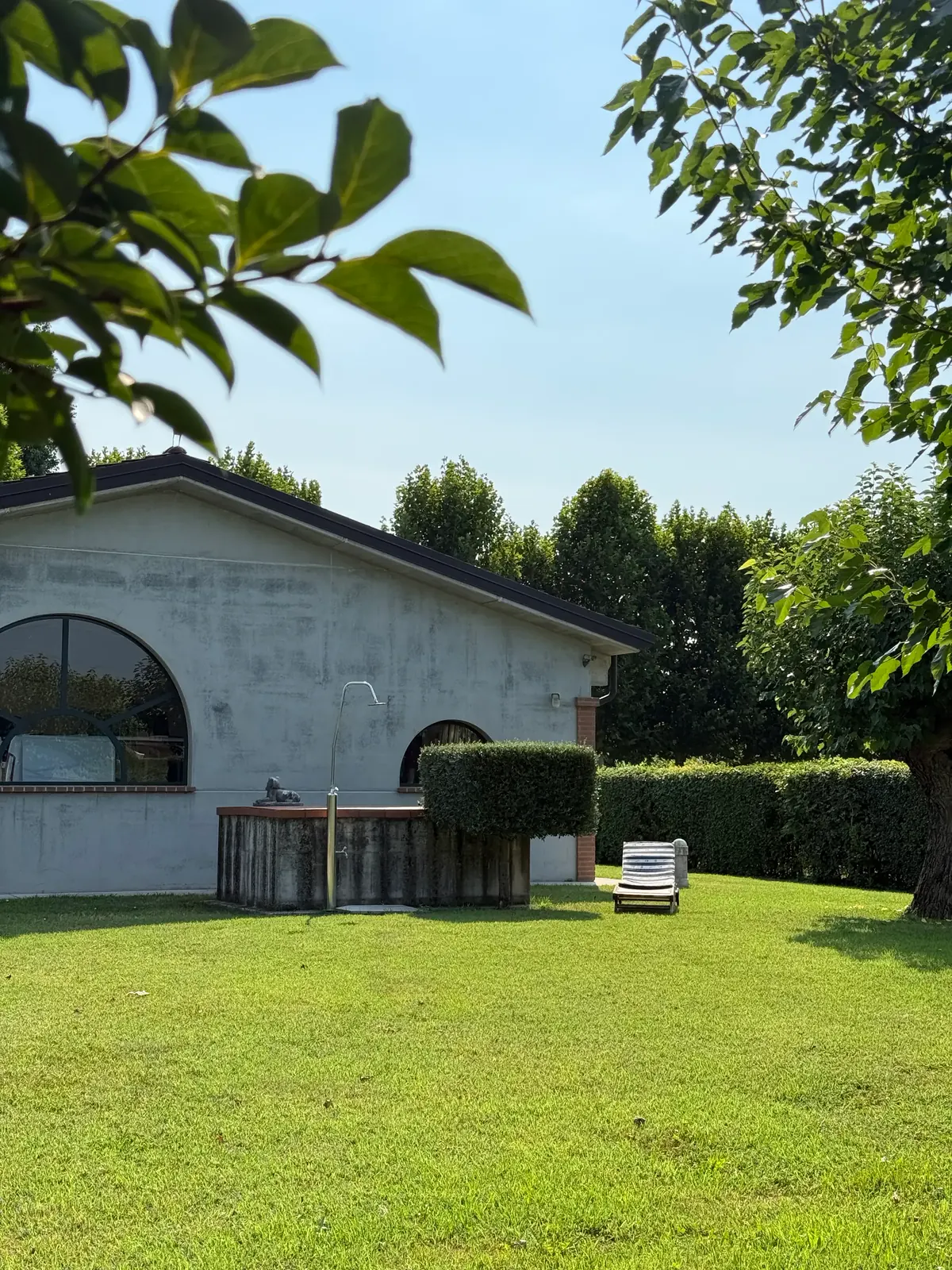 La casa con le finestre ad arco affacciata sul prato, tra siepi e alberi