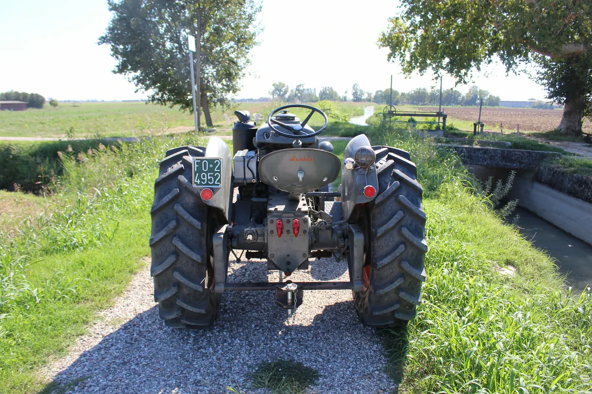 Il vecchio trattore visto da dietro sul sentiero in ghiaia lungo il canale, con la campagna aperta davanti