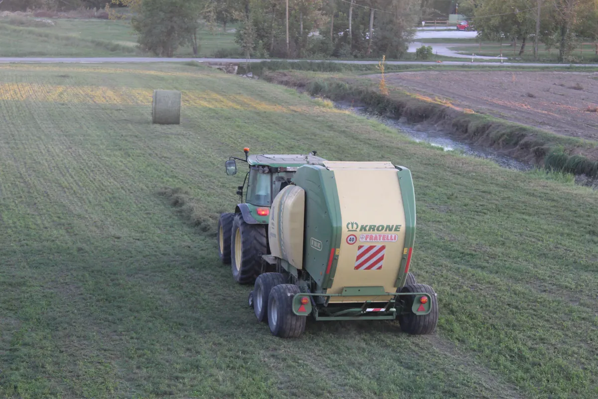 La rotopressa vista da dietro nel campo e, poco più in là, la prima rotoballa appena lasciata sull’erba, con il canale e la terra arata sullo sfondo
