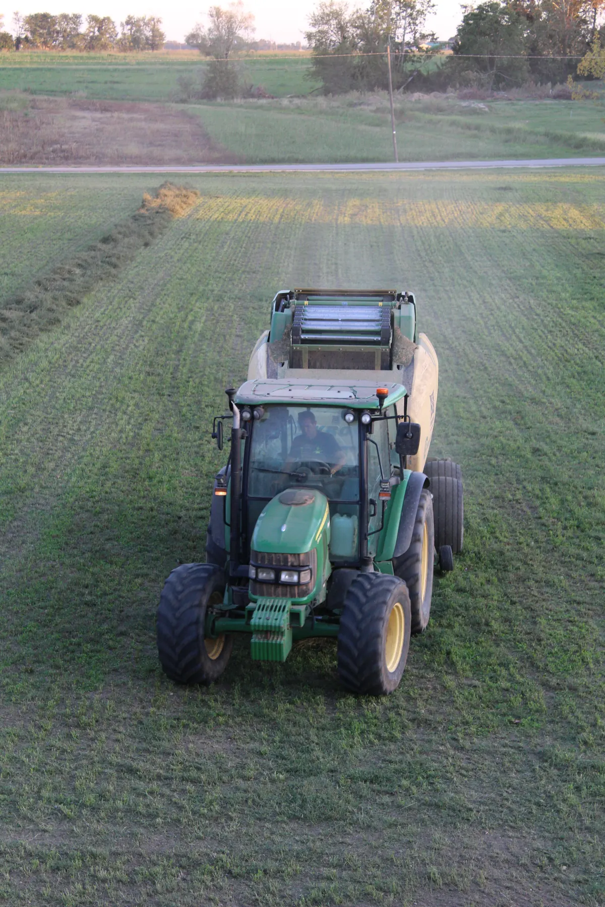 Il trattore verde con la rotopressa che avanza di fronte lungo un’andana, visto dall’alto